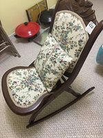 Full view of the wooden folding rocking chair with floral upholstery and matching throw pillow on the seat.