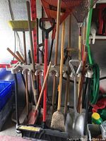 Front view of a beige cast lawn care caddy on wheels holding various garden tools including shovels, rakes, brooms and a garden hose.