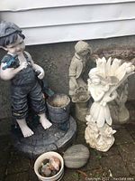 Overview of all lawn ornaments including cement boy statue, resin girl fairy statue, small bird bath, and stones in a bowl and loose.