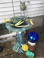 Overall view of teal metal bird bath on brick patio with assorted garden ornaments at base
