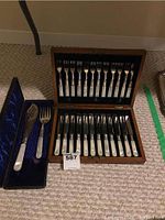 Full view of wooden case holding 12 forks and 12 knives with mother of pearl handles, plus separate blue satin-lined box with cake server and fork.