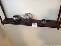 Photo of the bottom shelf with three glass items: art glass apple, multicolored glass paperweight, and small clear glass paperweight