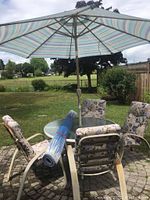 Photo showing round glass table with umbrella and four cushioned armchairs on brick patio with grass background.
