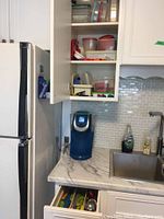 Kitchen corner with open cabinet showing assorted plastic food storage containers and Brita water filter on counter.