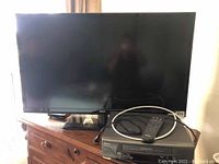 Full front view of RCA LED TV on wooden stand with Sanyo VCR and remote on top.