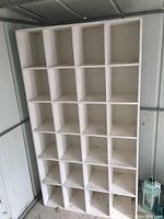 Front and side views of the homemade shelf unit displaying 25 square cubbies and visible wear.
