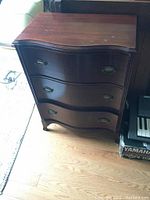 Front view of small bowed front dresser made of dark stained solid wood with three drawers and metal hardware.