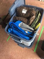 Photo showing a gray Rubbermaid storage container filled with four tarps in brown, blue, silver, and camouflage pattern.