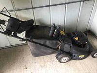 Side view of Yardworks lawn mower displaying black fabric grass catcher and two bottles of oil placed on top.