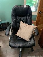 Front view of the larger black faux leather computer chair with a beige pillow in the seat.