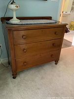 Front angled view of dresser showing three drawers, backsplash and turned bun feet