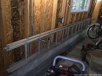 Side view of aluminum extension ladder against unfinished wall, ladder extended partially horizontally and elevated.