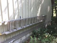 Collapsed aluminum extension ladder leaning against exterior siding