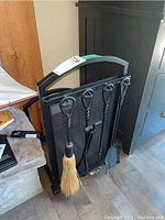 Front view of the black metal log rack with mesh screen and four fireplace tools hanging