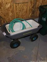 Yardworks garden cart with green hose coiled inside, showing general wear and stored inside a shed or garage.