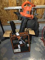 Orange Black & Decker electric leaf blower with attached bag resting on its original box, some wear visible on blower and box