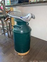 Front and side view of the painted dark green milk can bar stool with metal tractor seat and wooden base.