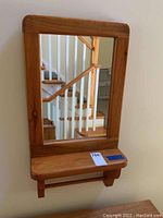 Front view of wooden framed mirror with shelf and towel bar.