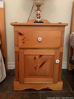 Front view of pine nightstand with drawer and cabinet door closed, showing wood grain and white knobs.