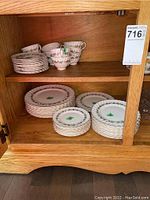 Porcelain dishes arranged on wooden shelves showing multiple stacks of plates and cups with floral leaf pattern and gold trim.