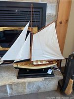 Full view of the model sail boat mounted on a black display base in front of a stone fireplace.