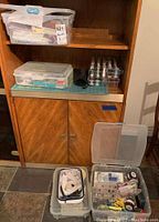 Three plastic storage bins on wood cabinet shelf and floor