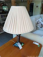 Full view of a table lamp showing beige pleated fabric shade and metal base on a wooden surface.