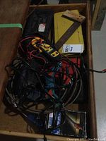 Drawer with assorted tools including a digital multimeter, yellow square, clamps, cables, and boxes.