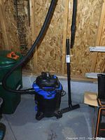 Photo of full shop vacuum unit showing hose connected and wand attached to wall.