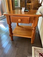 Side view of one wooden end table showing dovetail drawer and lower shelf with turned legs.