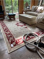Full view of cream and red floral wool rug in living room under ottoman and glider