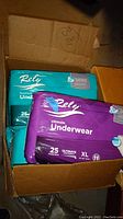 Photo showing two packages of Rely Ultimate Underwear adult diapers in teal and purple packaging inside a cardboard box.