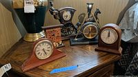 Wide view showing all four clocks on a wooden surface including the horse and carriage clock with lamp