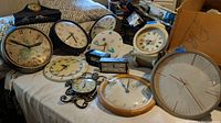 Wide shot of all clocks displayed on table showing variety of sizes, materials, and conditions