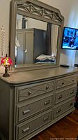 Front and slight side view of 6 drawer gray dresser with attached mirror and decorative carved frame top