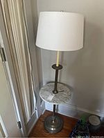 Full view of the metal floor lamp with marble-like table, white drum lampshade, base showing age marks.