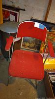 Front view of the red cloth folding chair with arm rests and metal frame.