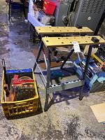 Photo of portable folding workbench with wooden top and metal legs, showing hole-punched surface and locking features, located in basement.