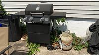 Full view of the black Range Master gas grill outdoors with attached propane tank showing rust and wear.