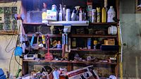 Photo of workshop wooden wall shelves with assorted hardware supplies, cleaners, and spray paint bottles
