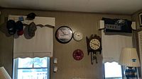 Wide shot showing multiple hats on wall-mounted rack, four different wall clocks including a Budweiser neon clock, a white round clock, a red clock, a Craftsman-style pendulum clock, and an Eagles towel.