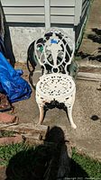 Front view of white cast iron outdoor chair showing decorative backrest and rust spots.