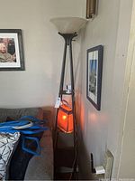 Tall shelf lamp with dark metal legs and frosted glass bowl shade, next to a couch and wall art. The purse-shaped lamp is hanging on the shelf part with an orange light.
