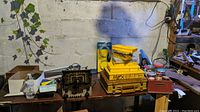 Overview of workbench with various tools, radio parts, yellow hex-key boxes, and hardware components arranged on the table