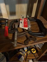 Photo showing several metal C-clamps of various sizes including one with red handle and a newly packaged clamp.