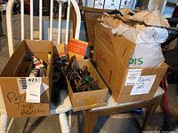 Photo showing three cardboard boxes on a white chair containing tubes of paint, wires, lamp posts, gloves, and an instruction booklet.
