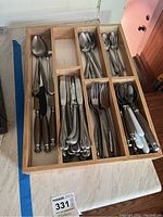 Wooden flatware organizer containing multiple types of flatware including spoons, forks, knives with varied handles.