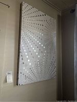 Large canvas wall art hanging on wall, showing pattern of raised silver dots radiating on beige to taupe canvas