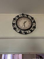 Black metal wall clock with floral accents on circular frame, mounted above doorway.