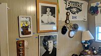 Wall of mixed items including framed posters, mirror, clock, Eagles decoration, coat rack, hats, and lamp